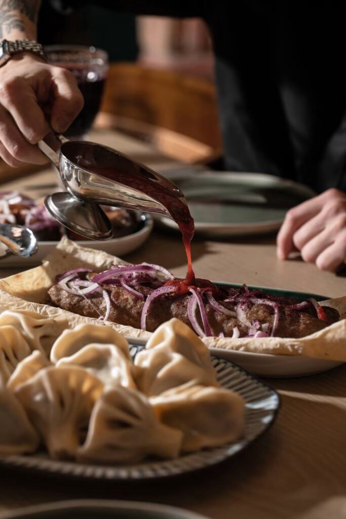 Kebab and khinkali on the Vakhtanguri table, sauce being poured over the meat